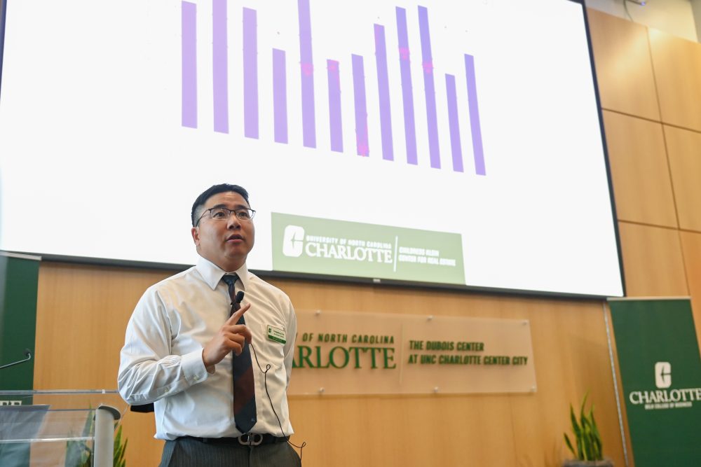 Dr. Yongqiang Chu presenting his findings in a large auditorium with a bar graph up on the screen behind him