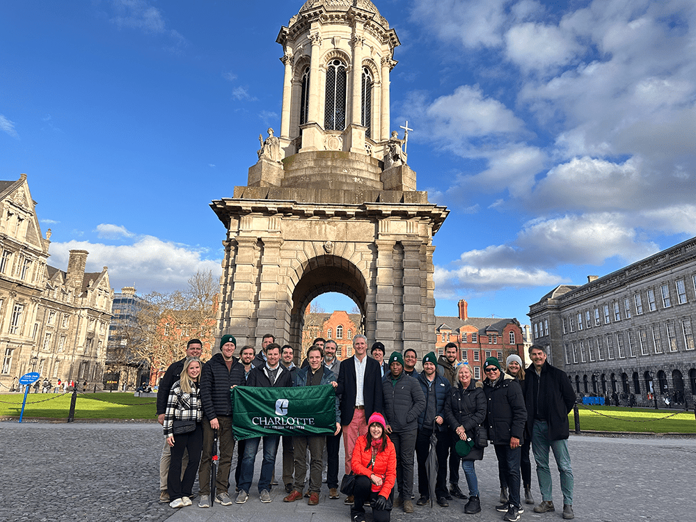 Students and faculty on a study abroad trip posing with a green UNC Charlotte flag