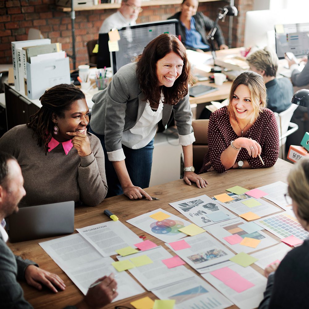 Management Programs: organizational management concentration. Group of co-workers standing and sitting around a large table working on an organizational project.