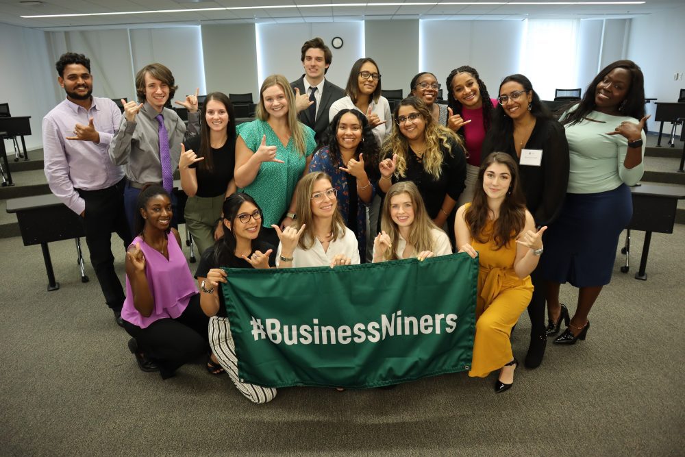 UNC Charlotte's M.S. in Management cohort holds a "#BusinessNiners" green banner