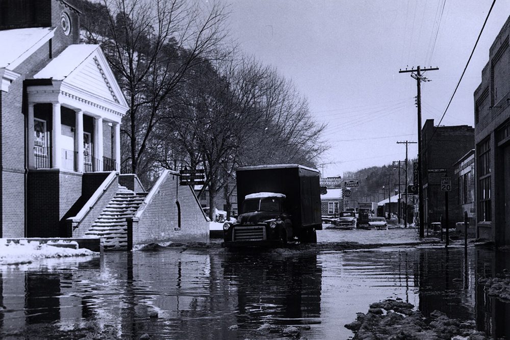 As snow melts in 1958, South Main Street in front of Marshall Presbyterian Church is awash with water. The new church building was constructed with the sanctuary on the second floor, after flooding of the previous church building. Image: Southern Appalachian Digital Collections.