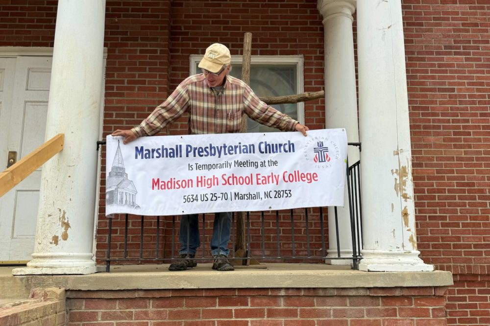 Man hanging sign in front of Marshall Presbyterian Church, noting the temporary site provided to the church at Madison County Early College